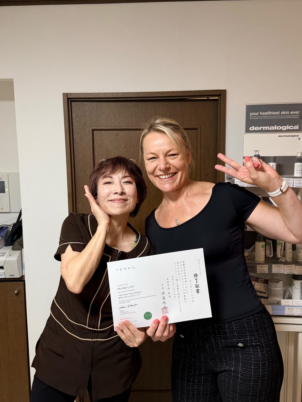 Michelle LynchさんがBody Stress Release™（ボディストレスリリーブ®︎）の修了証を受け取り、Amyと記念写真を撮る様子